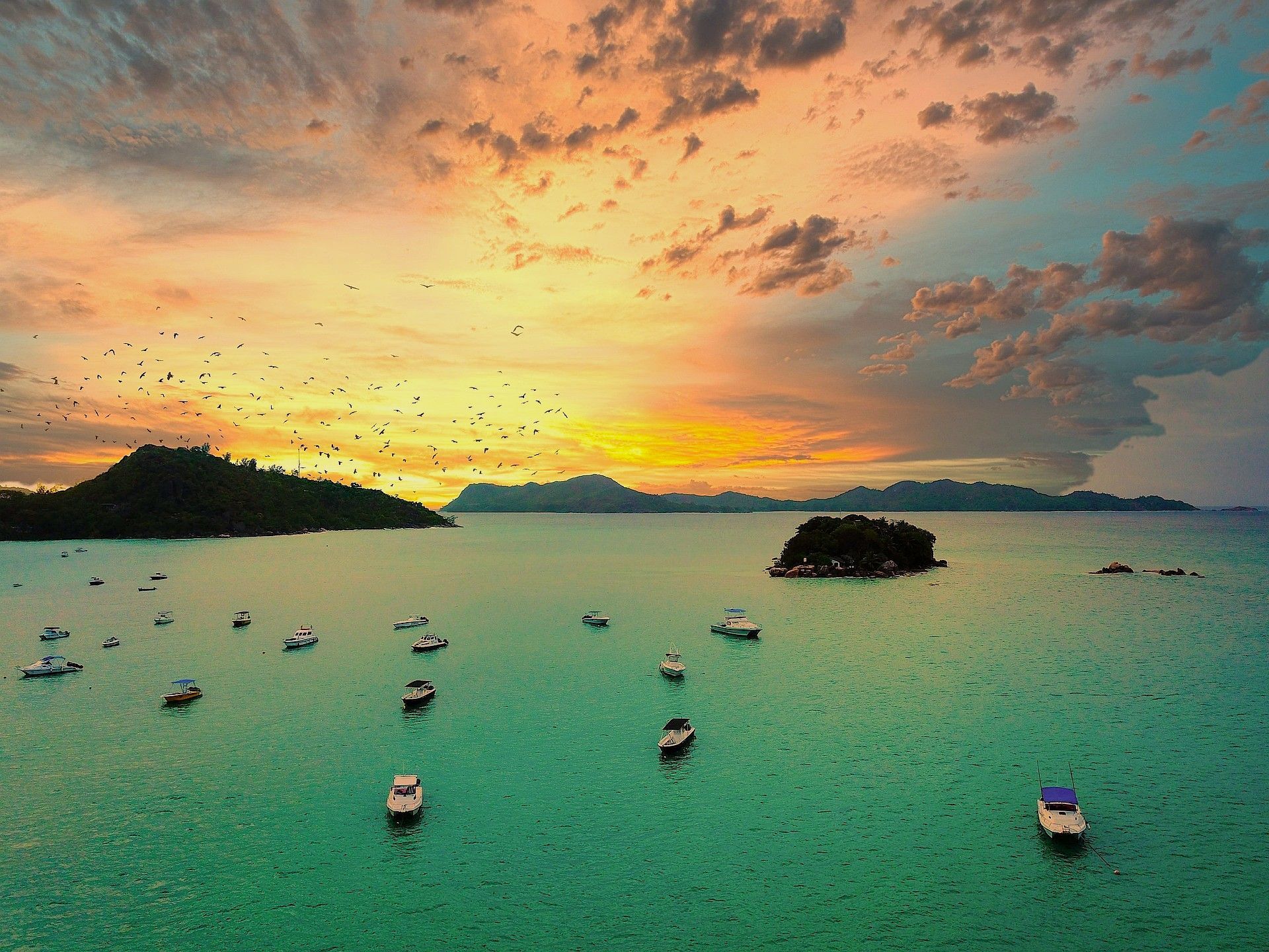 Sunset over ocean with boats, seychelles islands, and a colorful sky.