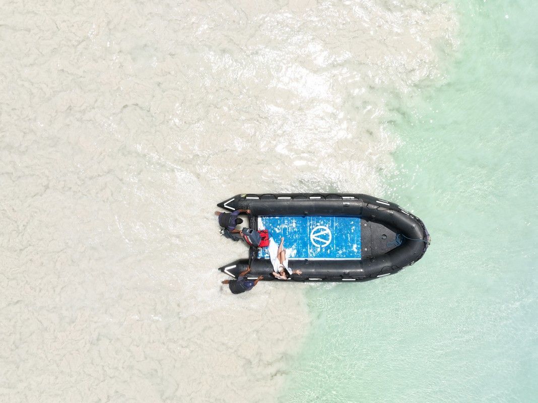 Black inflatable boat with two people on clear turquoise water.