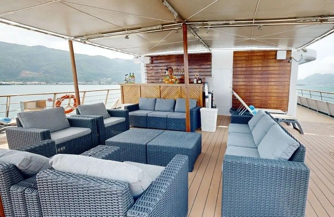 Outdoor lounge area on a boat with gray wicker furniture, bar, and ocean view.