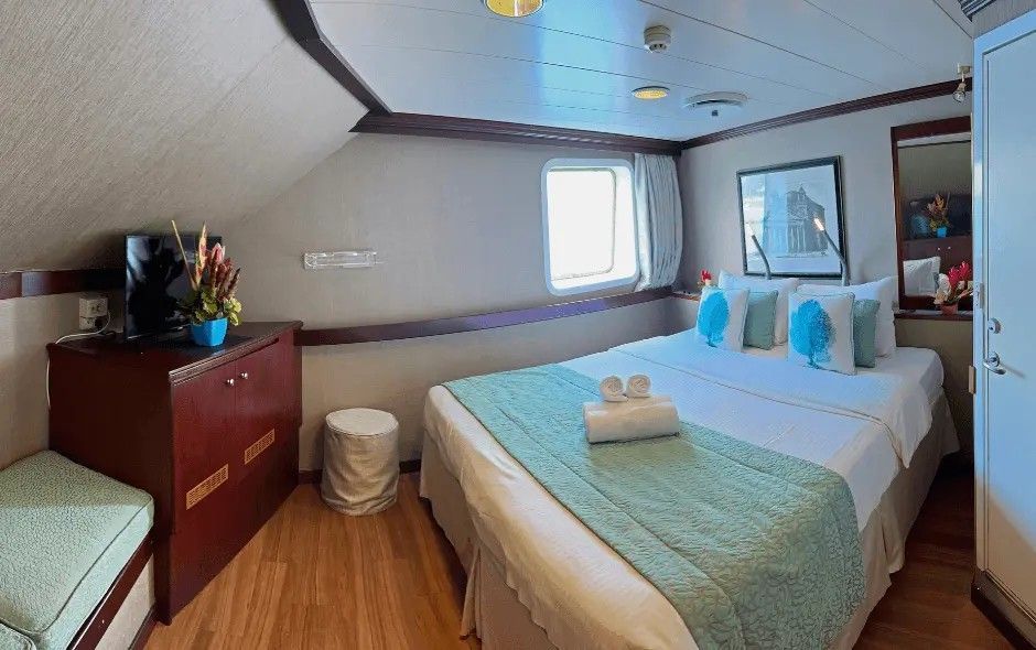 Cozy cabin on a ship with a bed, dresser, window, and seating. Turquoise and wood tones.
