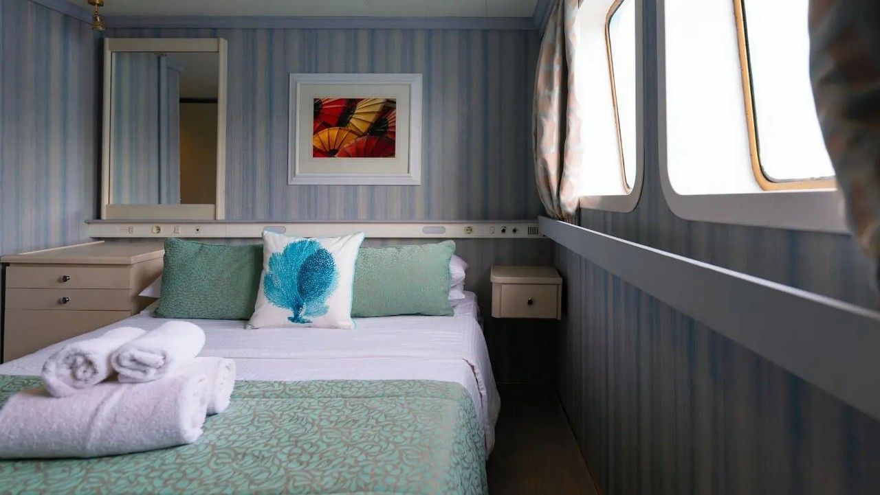 Bedroom on a boat with a bed, pillows, and window, blue and white color scheme.