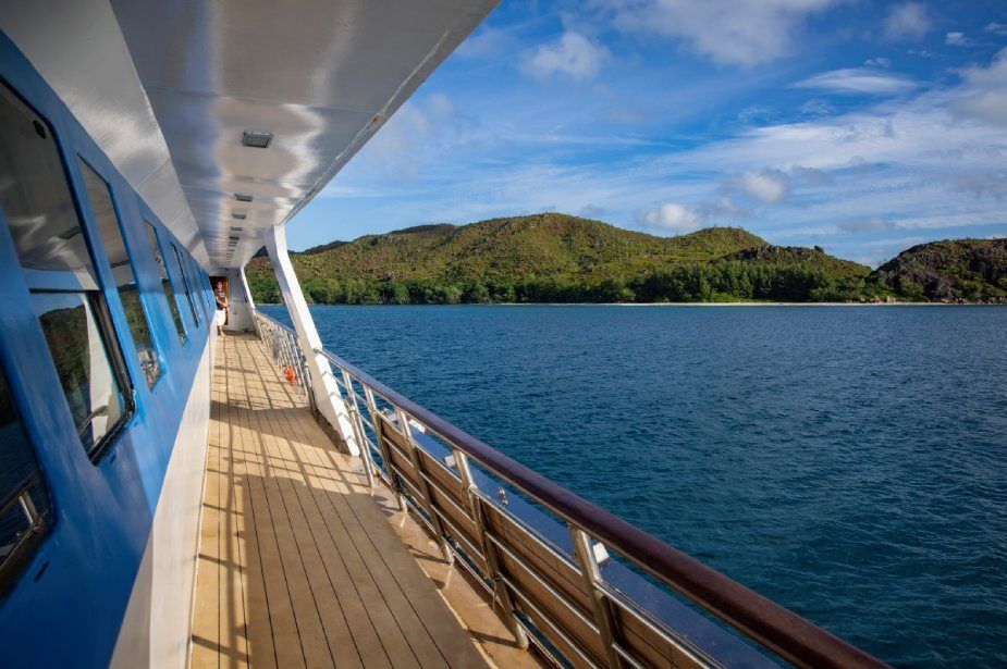 Boat sailing on blue water near a lush green island under a blue sky.