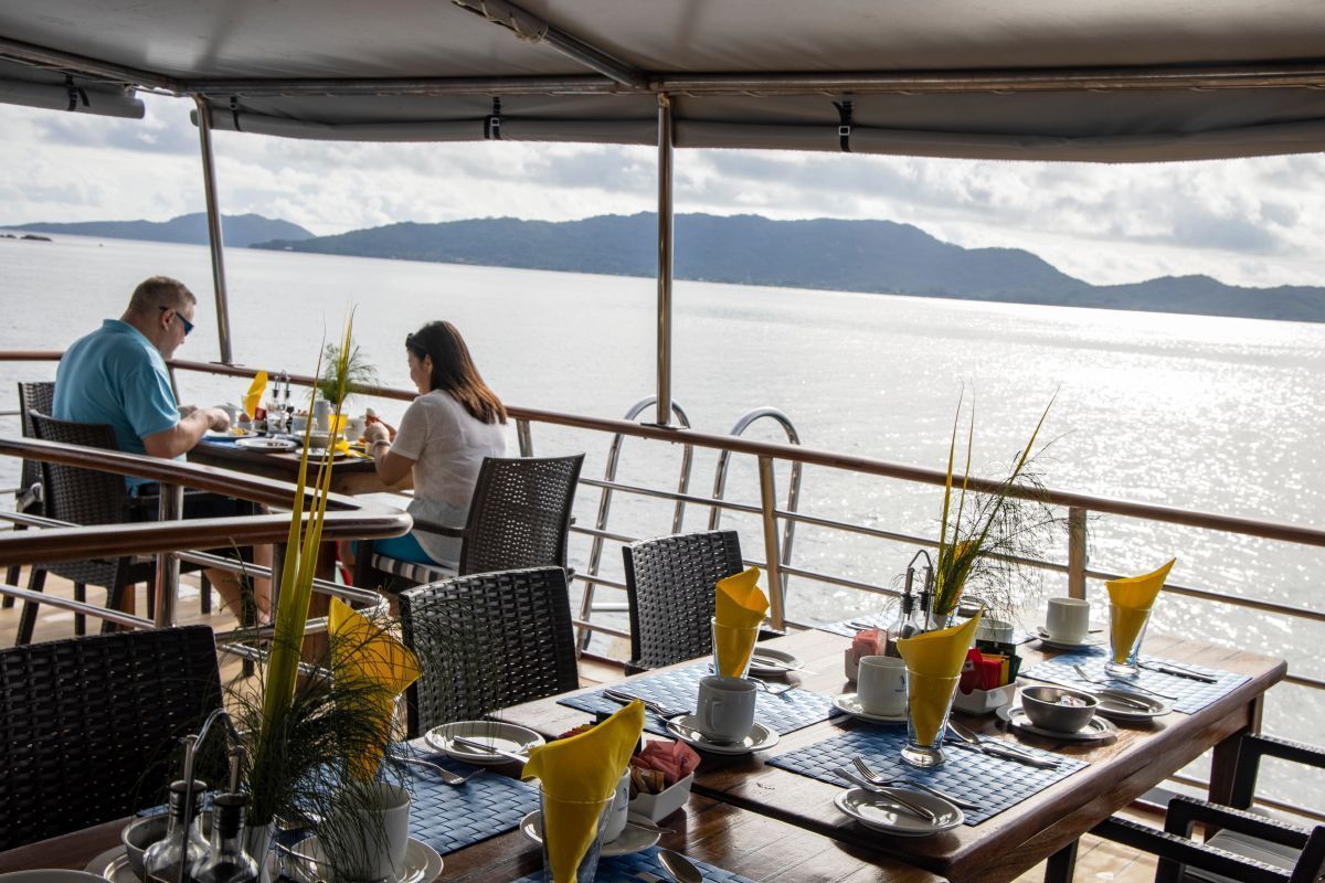 Couple dining at a waterside restaurant with a scenic ocean and mountain view.