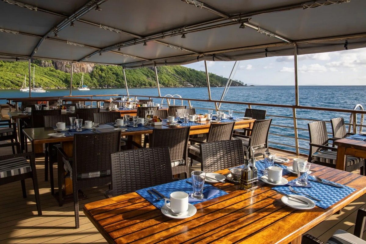 Outdoor dining tables set with blue linens on a boat, ocean view.