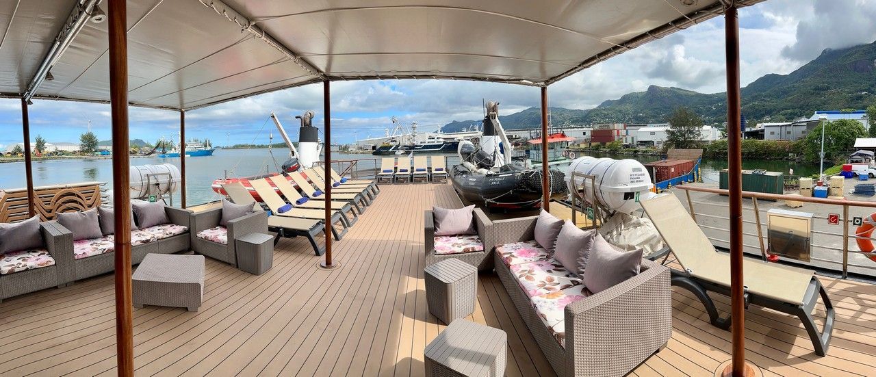 Outdoor lounge area with gray couches, chaise lounges, and a harbor view.