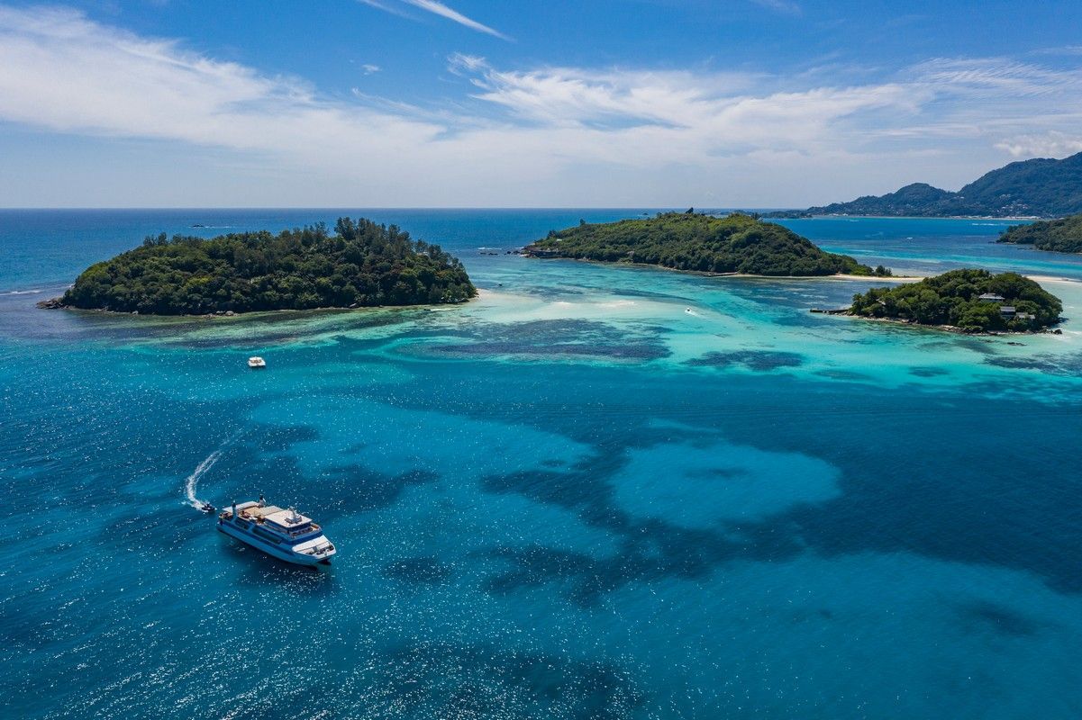 Bright blue ocean with a boat near small, green islands under a sunny sky.