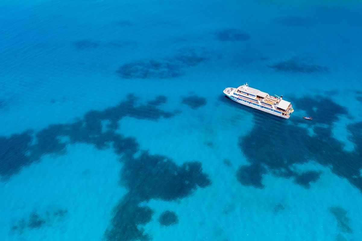 Swim stop in the Seychelles White boat on turquoise water, surrounded by dark patches; aerial view.