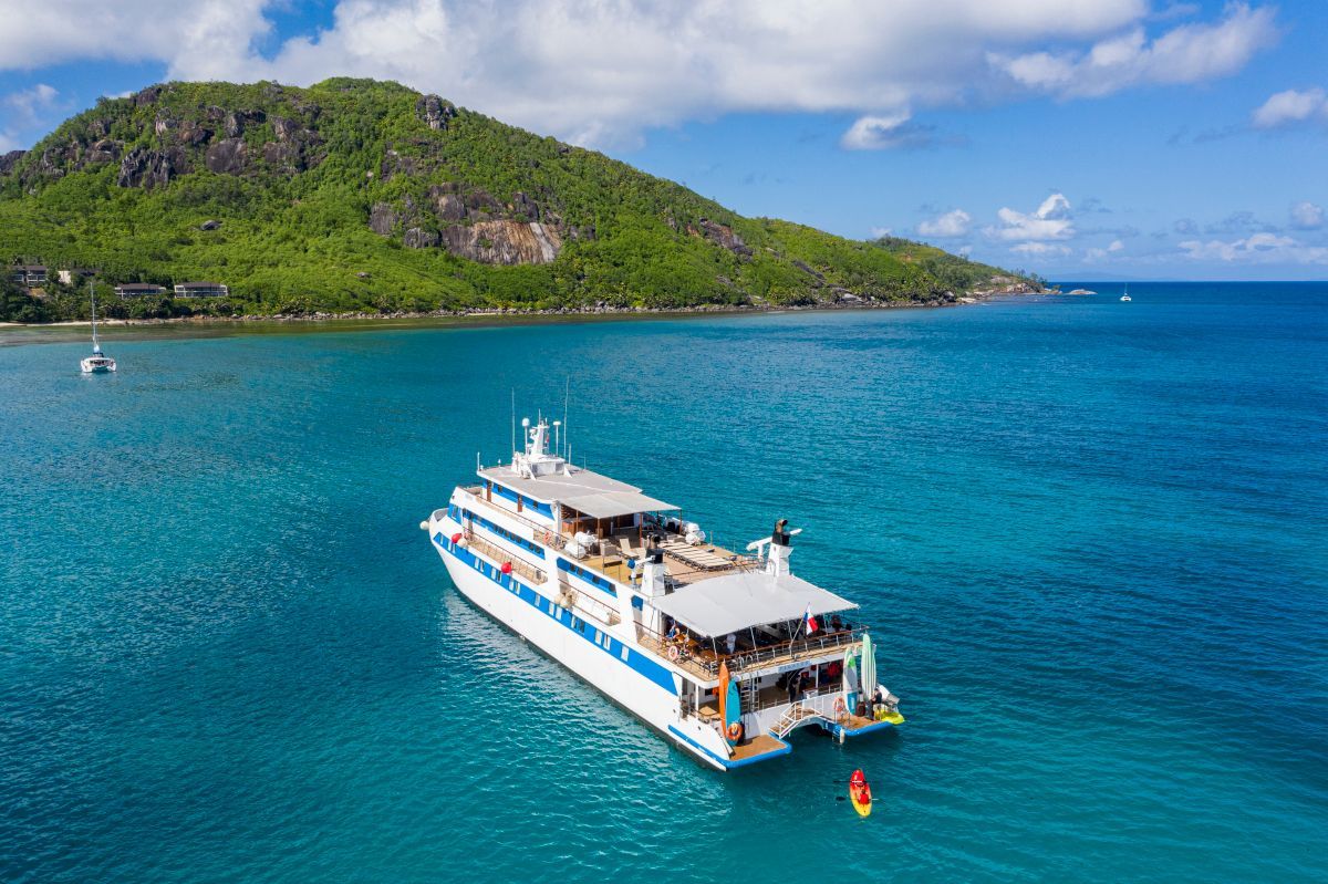 M/Y Pegasos A large white and blue catamaran in turquoise water near a lush, green island under a blue sky.