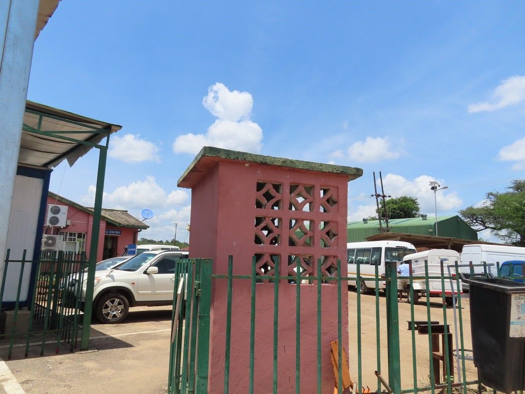 A pink telephone booth is behind a green fence in a parking lot.
