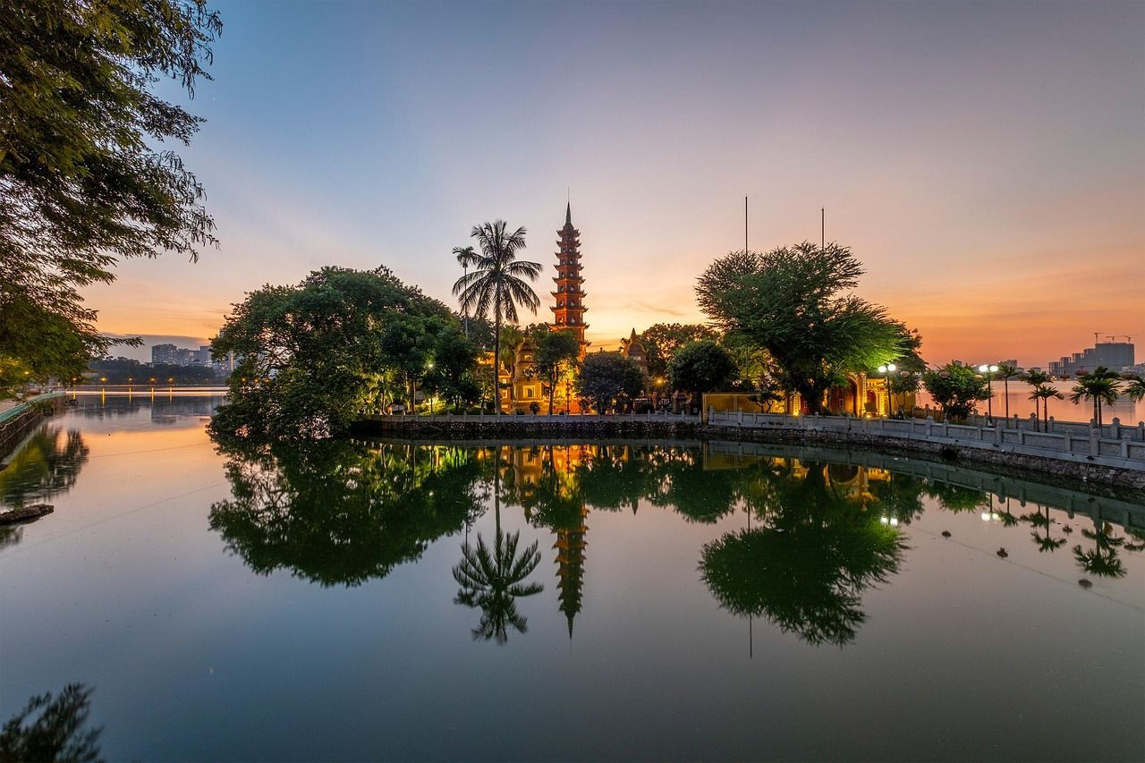 Sunset over Tran Quoc Pagoda in Hanoi, Vietnam, reflected in calm water.