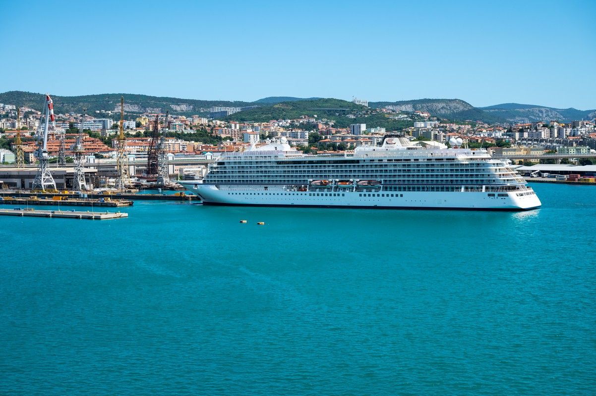 A viking cruise ship is docked in a harbor with a city in the background on a world cruise.