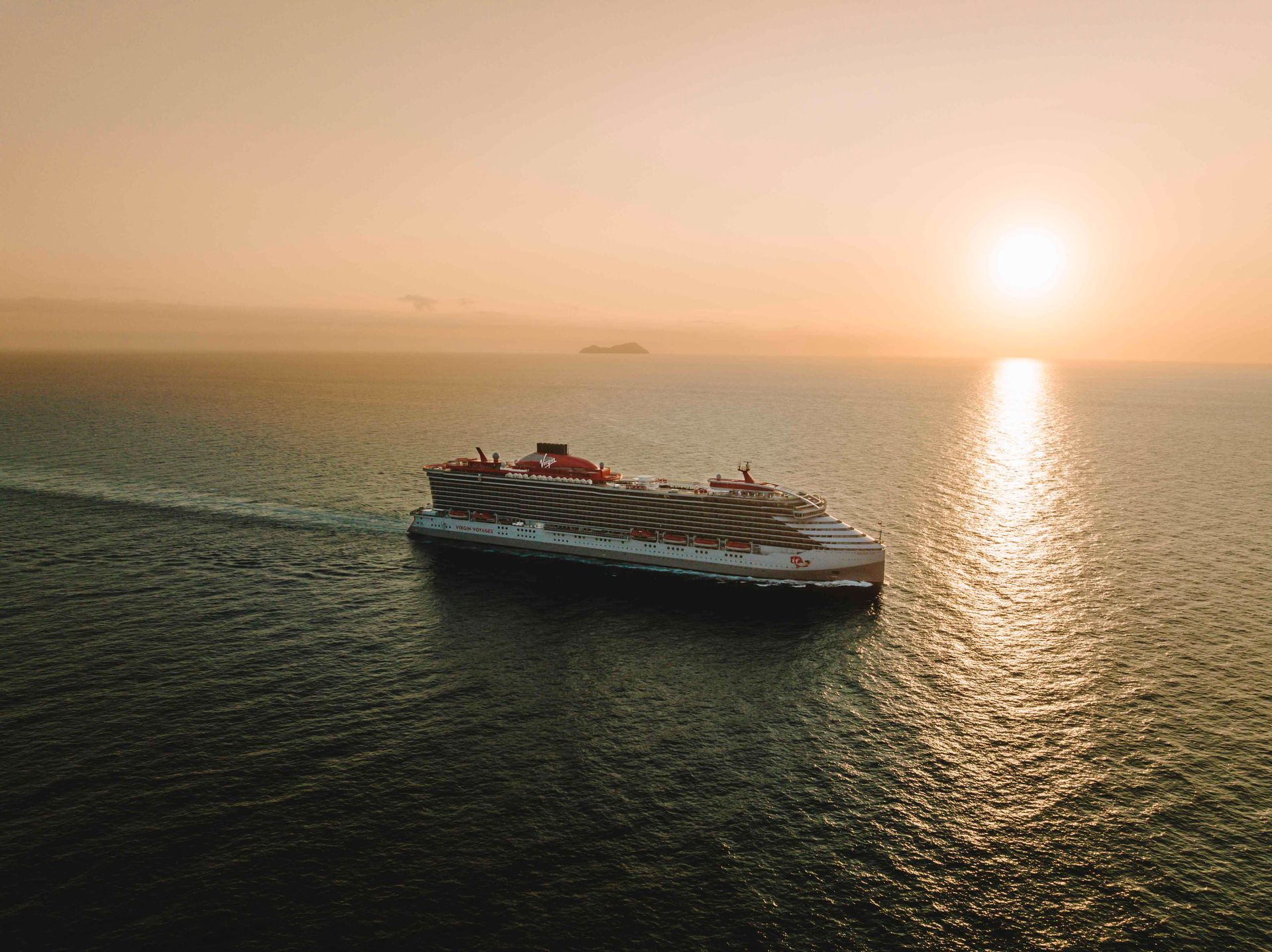 An aerial view of a virgin voyages cruise ship in the ocean at sunset.