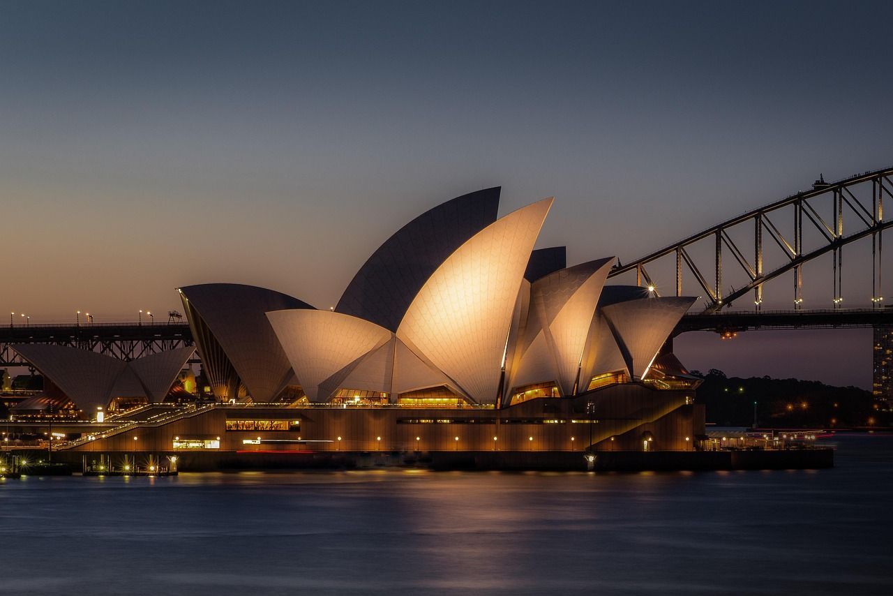 The sydney opera house is lit up at night with a bridge in the background on the Princess Cruises 2027 World Cruise