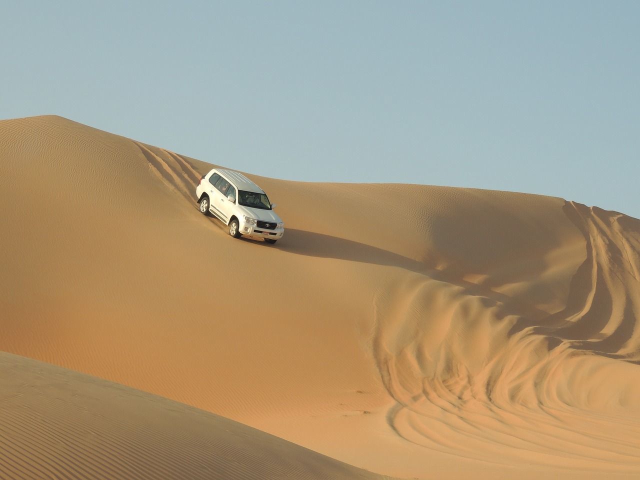 A white suv is driving down a sand dune in the desert