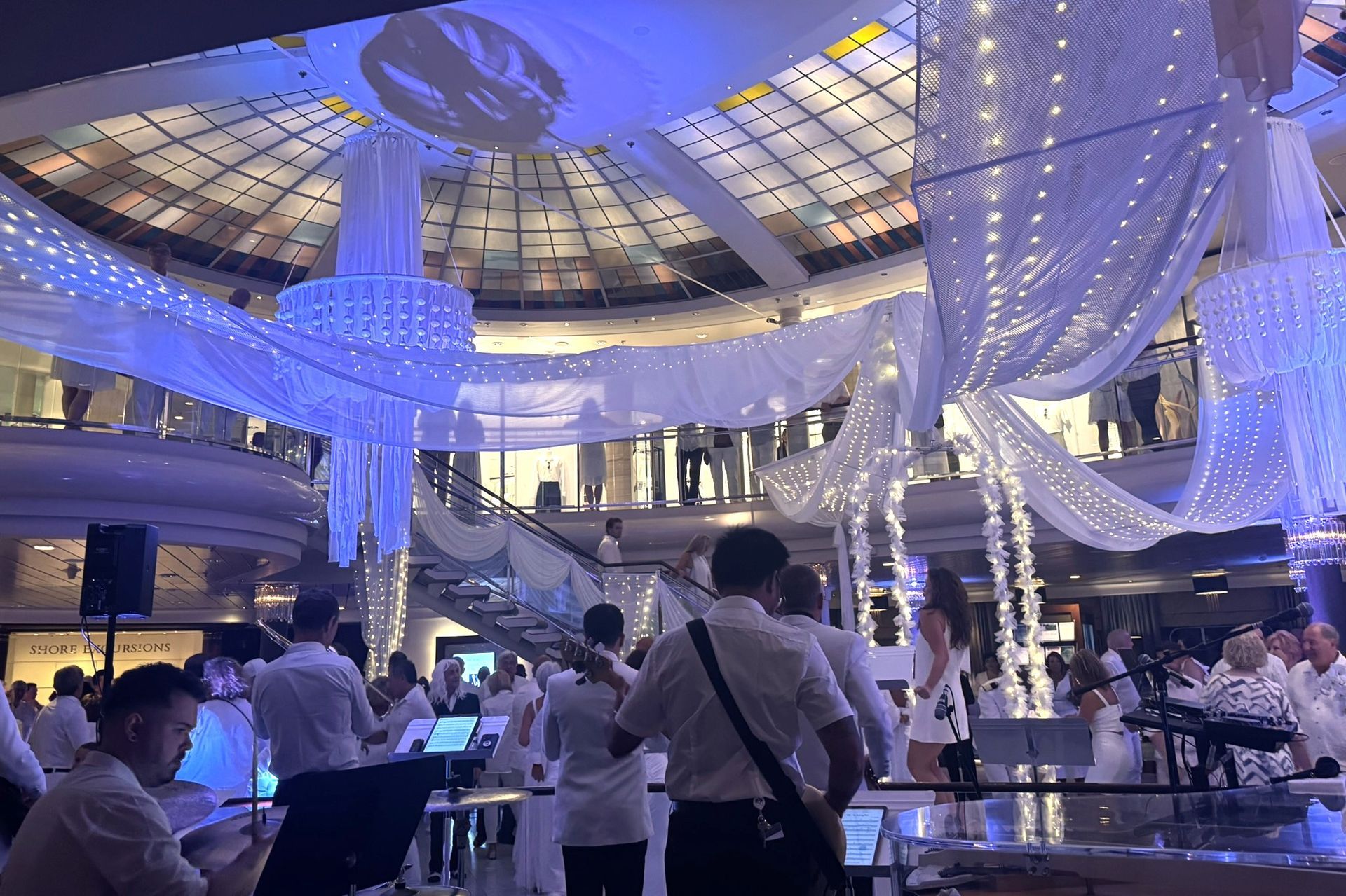 Band performs in a bright, white decorated atrium with white clothing and blue lighting.