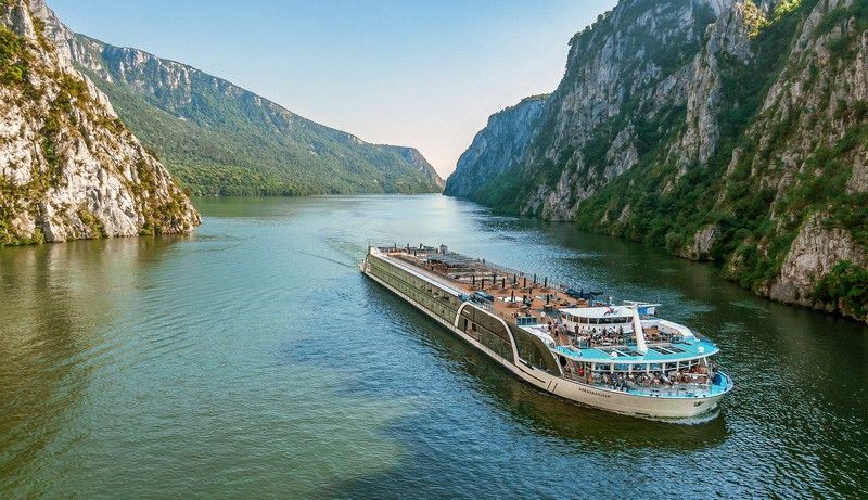 a river cruise ship is floating down a river surrounded by mountains .