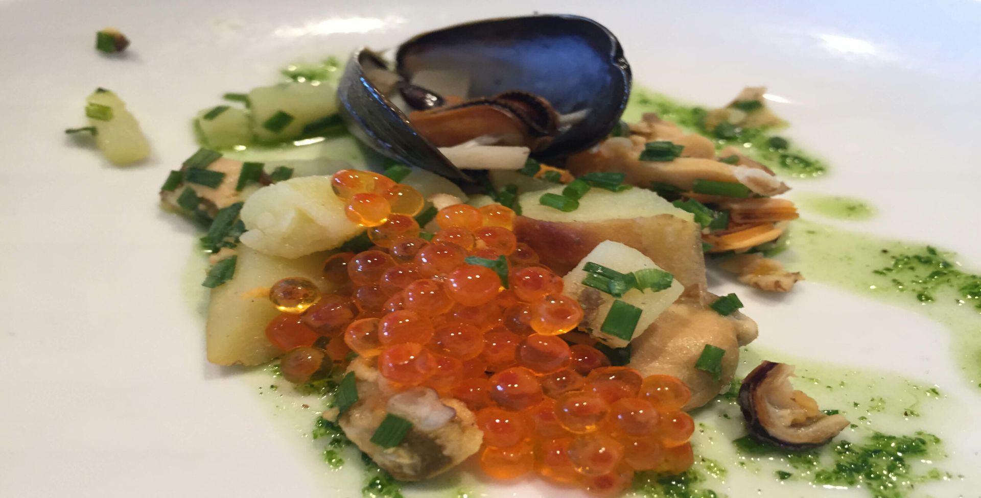 A close up of a plate of food with red caviar and clams.
