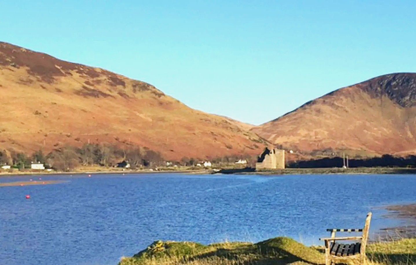 Isle of Arran Lake with mountains, stone castle ruins, and a bench in a scenic Scottish landscape.
