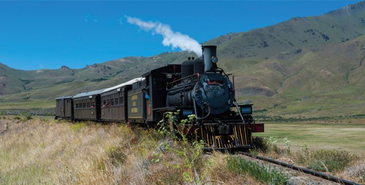 A train is going through a field with mountains in the background.