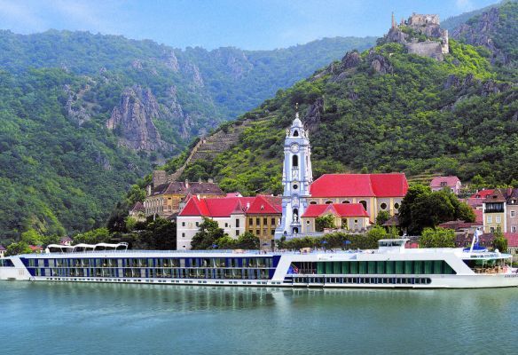 A river cruise ship is docked in front of a small town on a river.