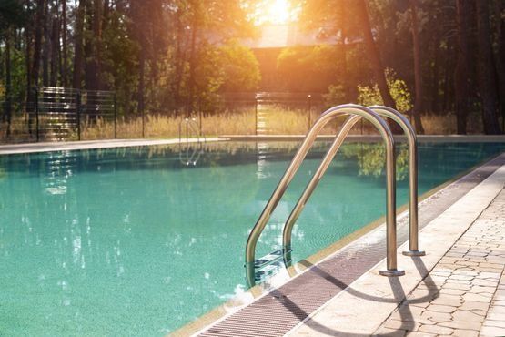 Una piscina con escaleras que conducen a ella y el sol brillando a través de los árboles.