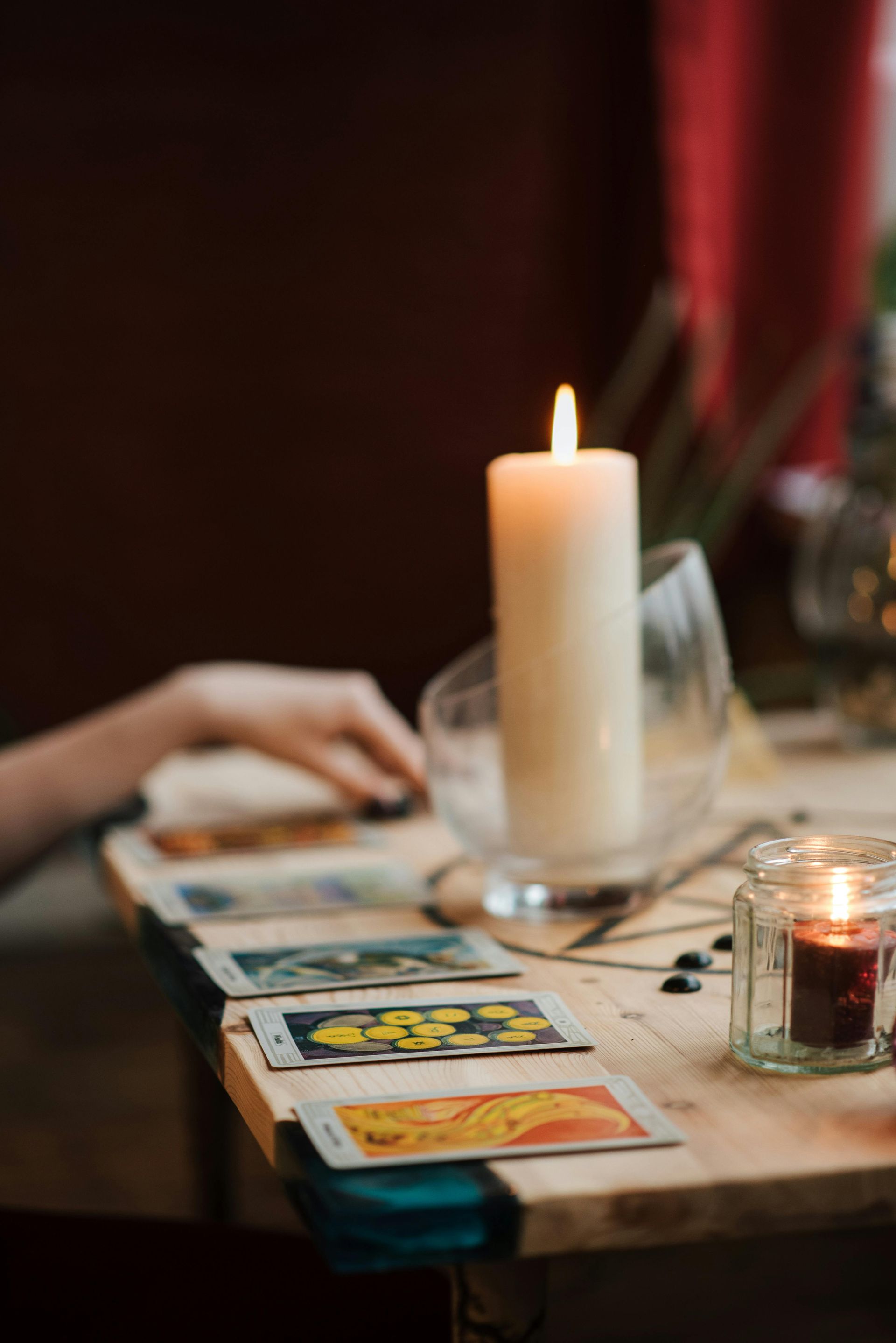 Mano de persona con esmalte de uñas negro cerca de cartas del tarot, velas encendidas sobre una mesa de madera.
