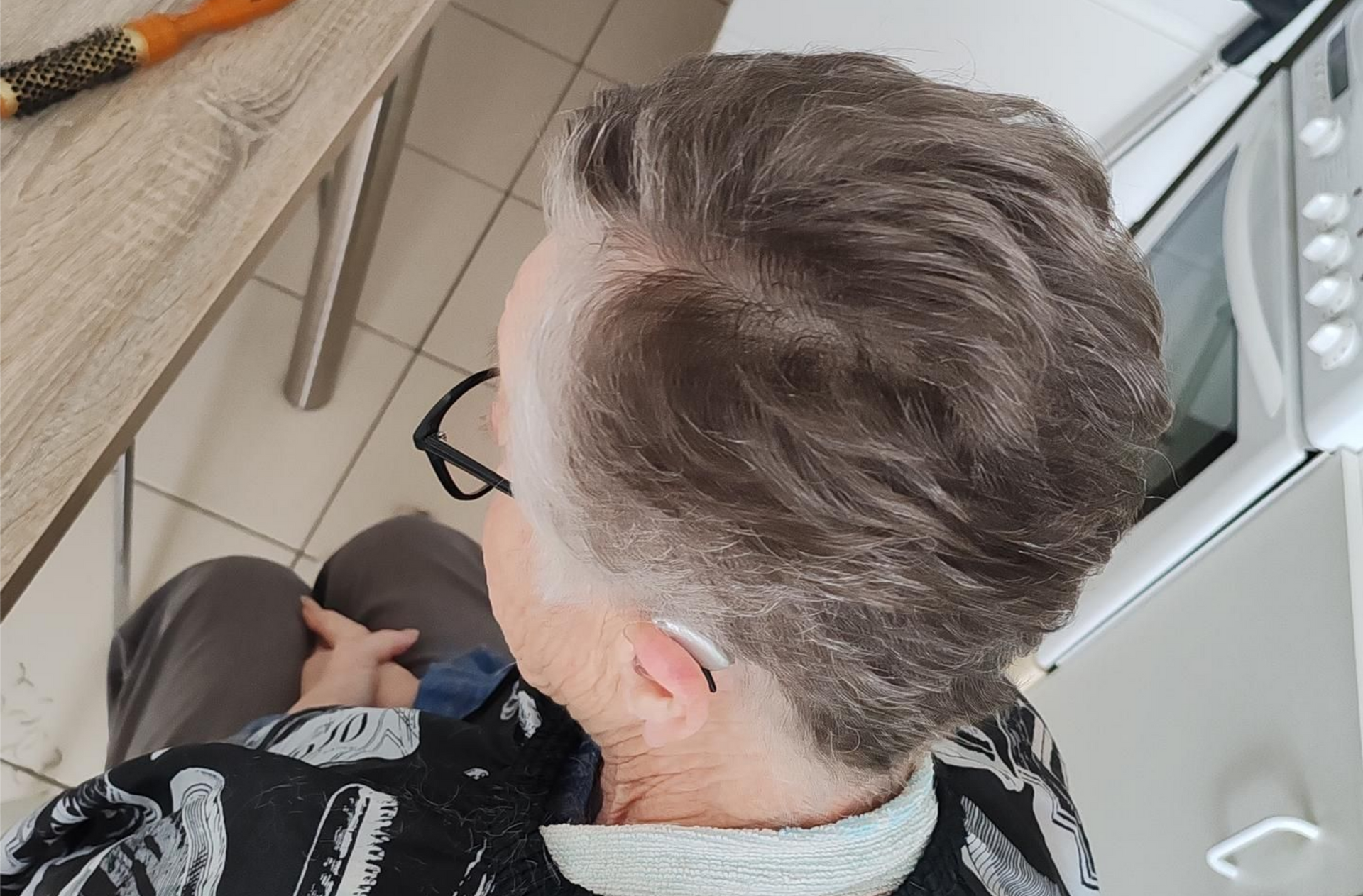 Personne aux cheveux gris courts et ondulés assise sur une chaise.