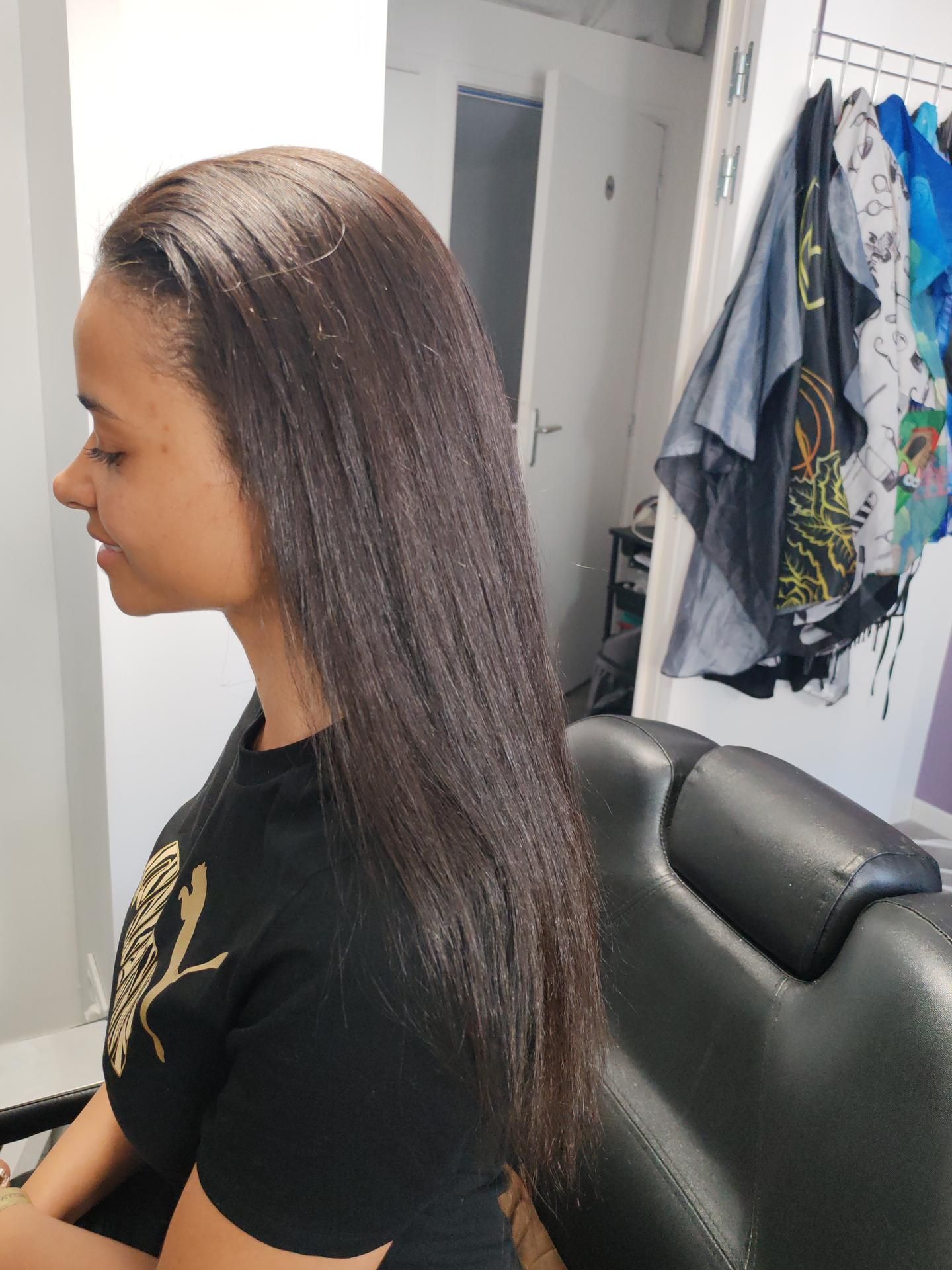 Femme aux cheveux noirs, lisses et brillants. Elle est assise dans un fauteuil de salon.