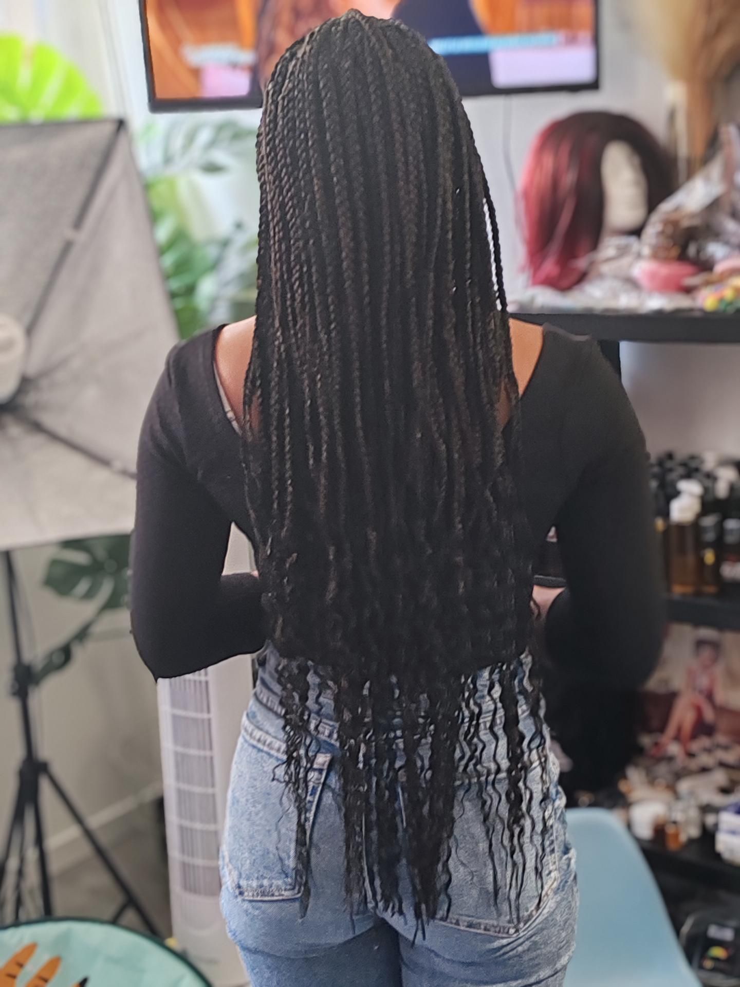 Une personne aux longues tresses noires tressées dans un salon de coiffure.