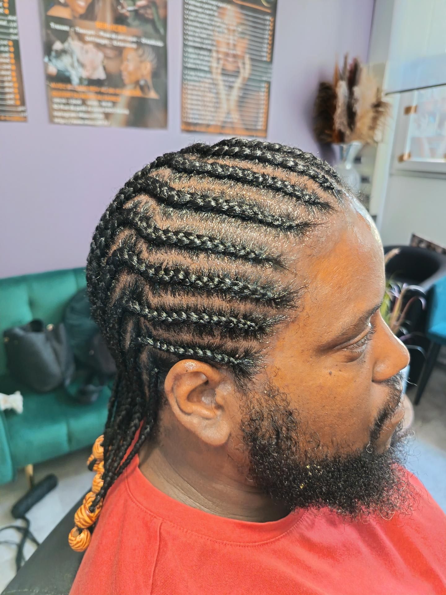 Un homme aux cheveux tressés et à la barbe fournie est assis dans un salon de coiffure.