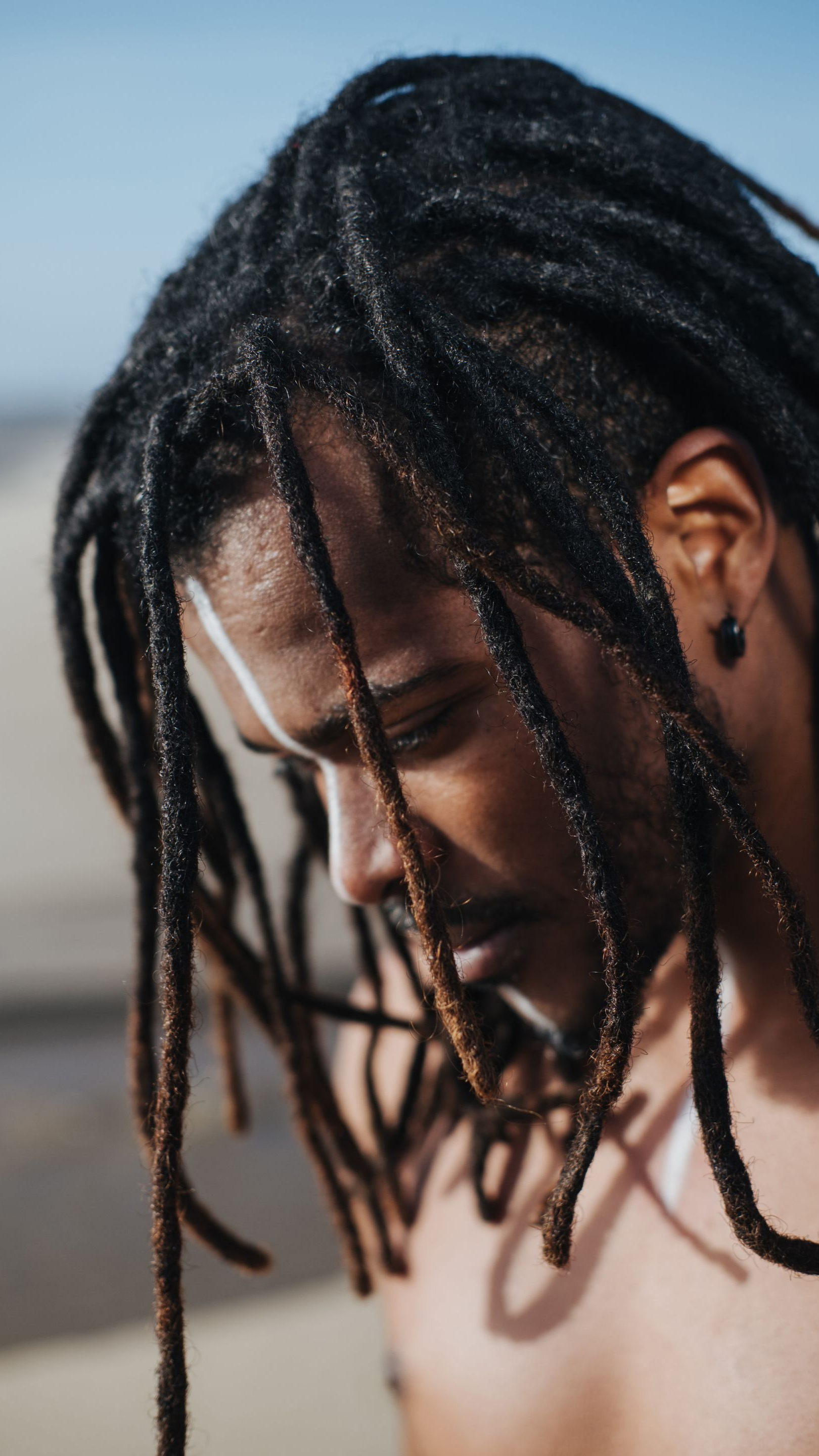 Homme aux dreadlocks regardant vers le bas en extérieur.