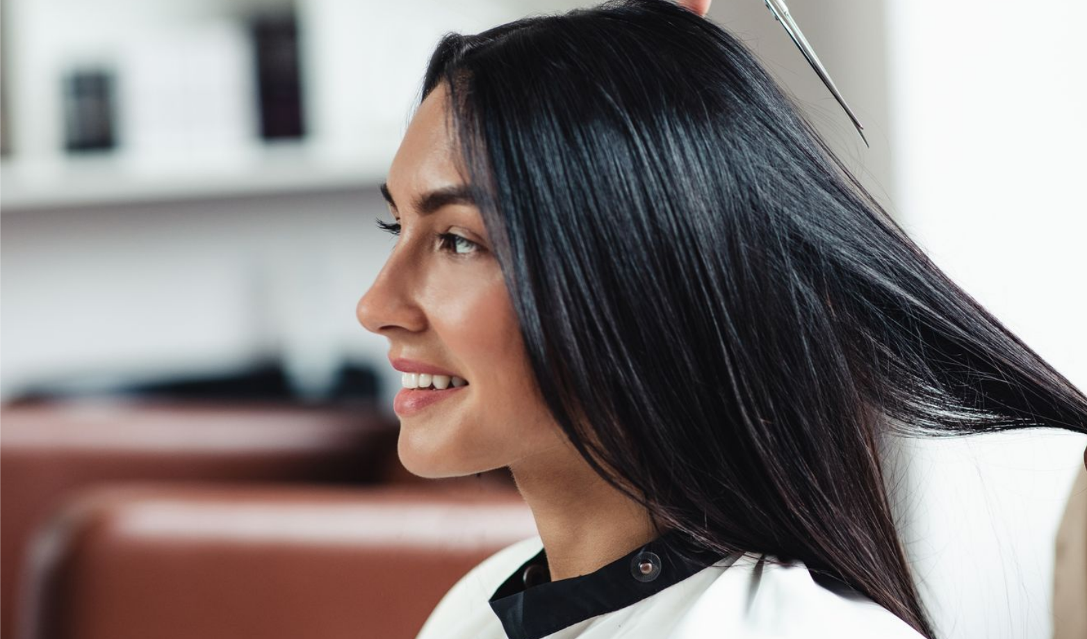 Femme aux longs cheveux noirs, souriante, se faisant coiffer dans un salon de coiffure.