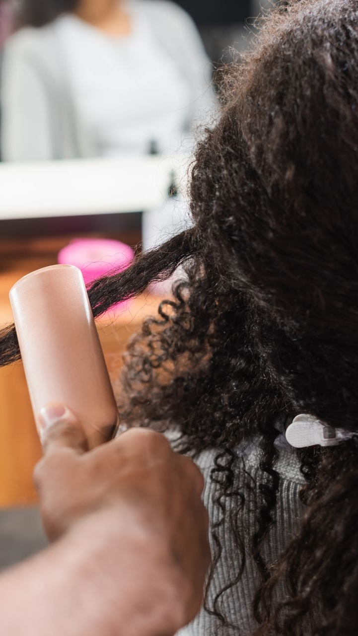 Coiffeur utilisant un produit sur cheveux bouclés en salon.