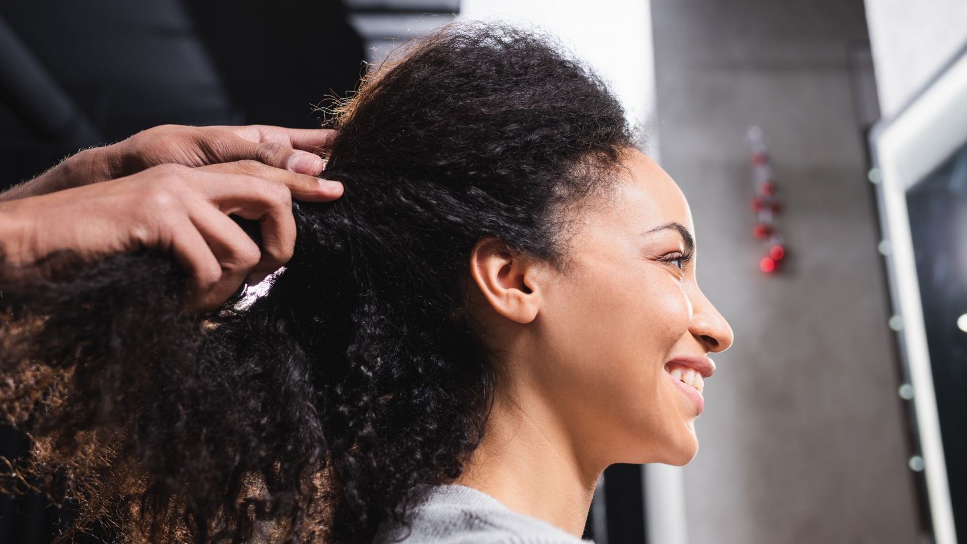 Une main coiffe une femme avec des cheveux foncés et bouclés dans un salon de coiffure.