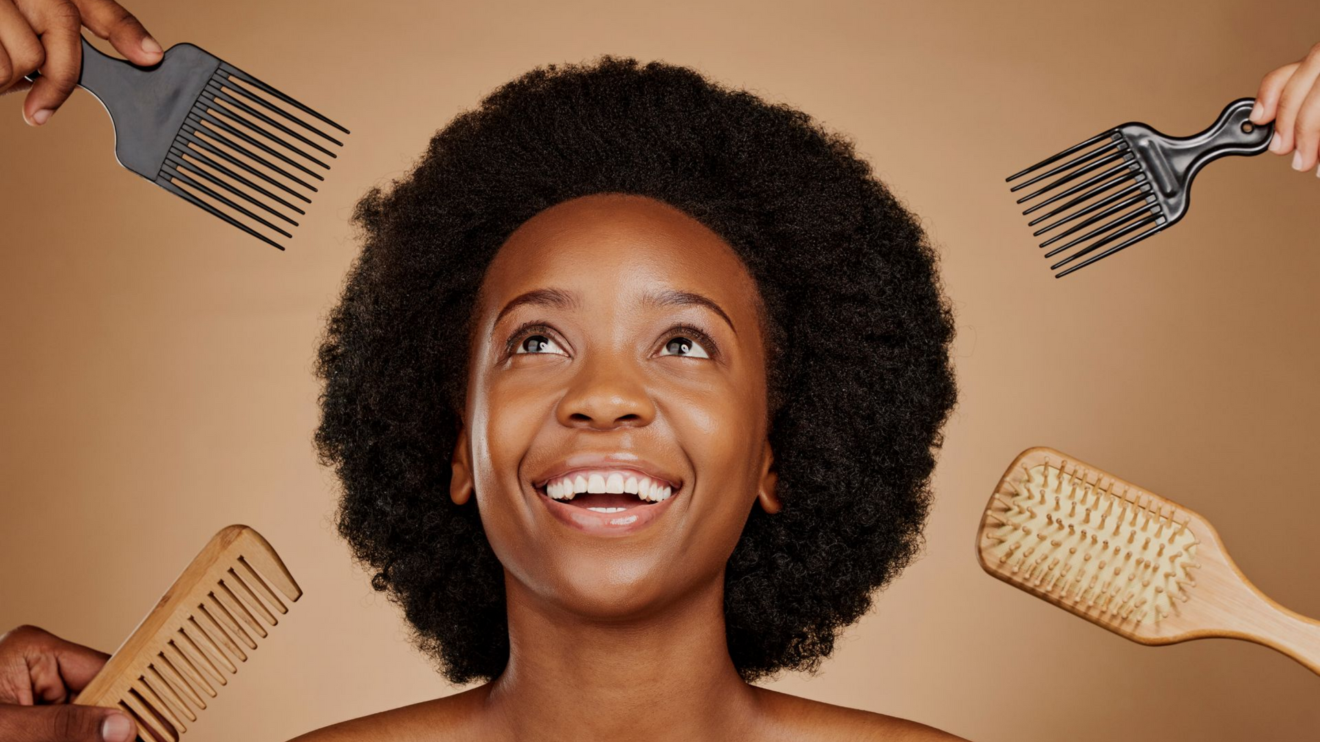 Une femme aux cheveux naturels sourit, entourée de quatre mains tenant des outils de coiffure.
