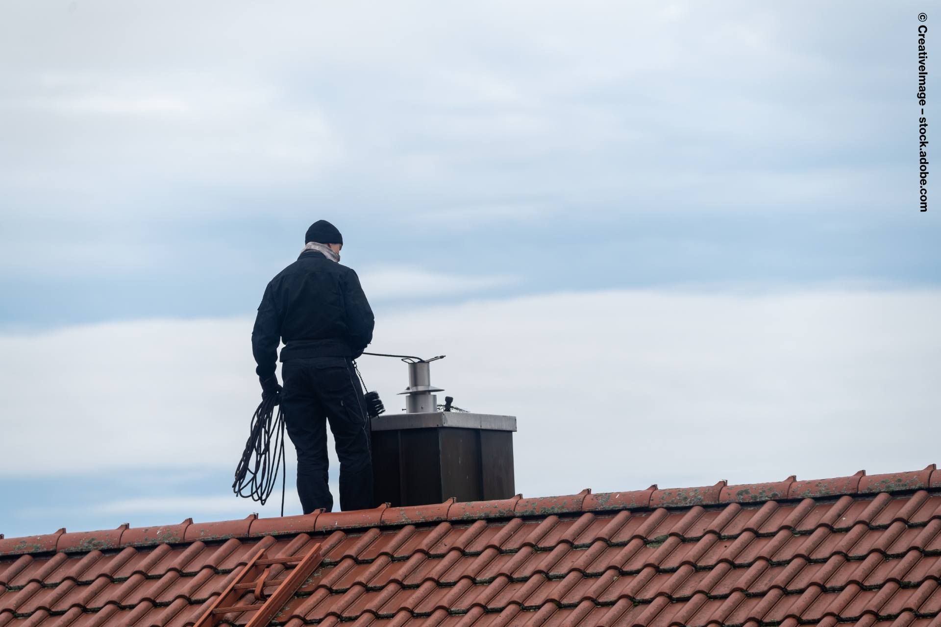 Schornsteinfeger macht einen Schornstein auf dem Dach sauber