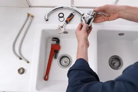 Un fontanero está arreglando un grifo en un fregadero de cocina.
