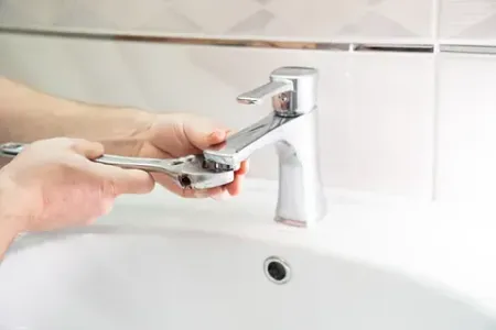 Una persona está arreglando un grifo del fregadero con una llave inglesa.