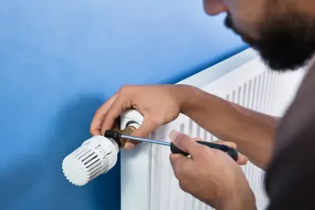 Un hombre está arreglando un radiador con un destornillador.
