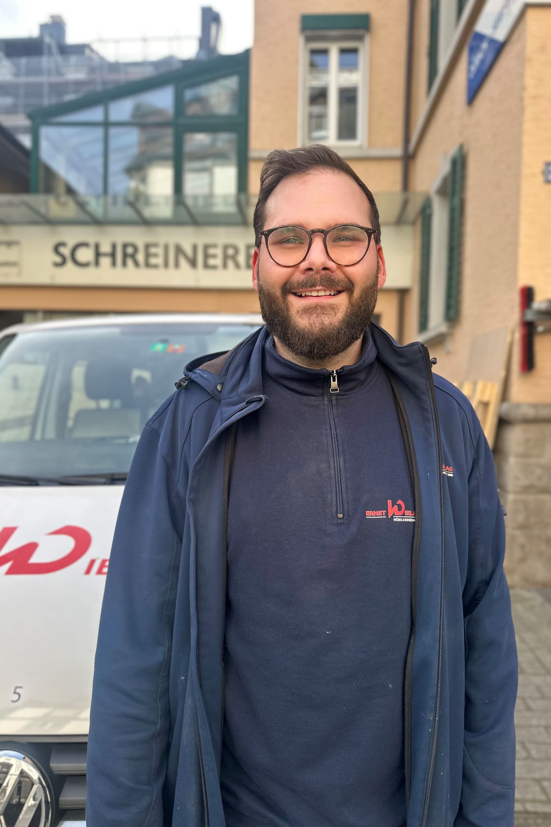 Ein Mann mit Brille und Hut lächelt vor einem Lieferwagen