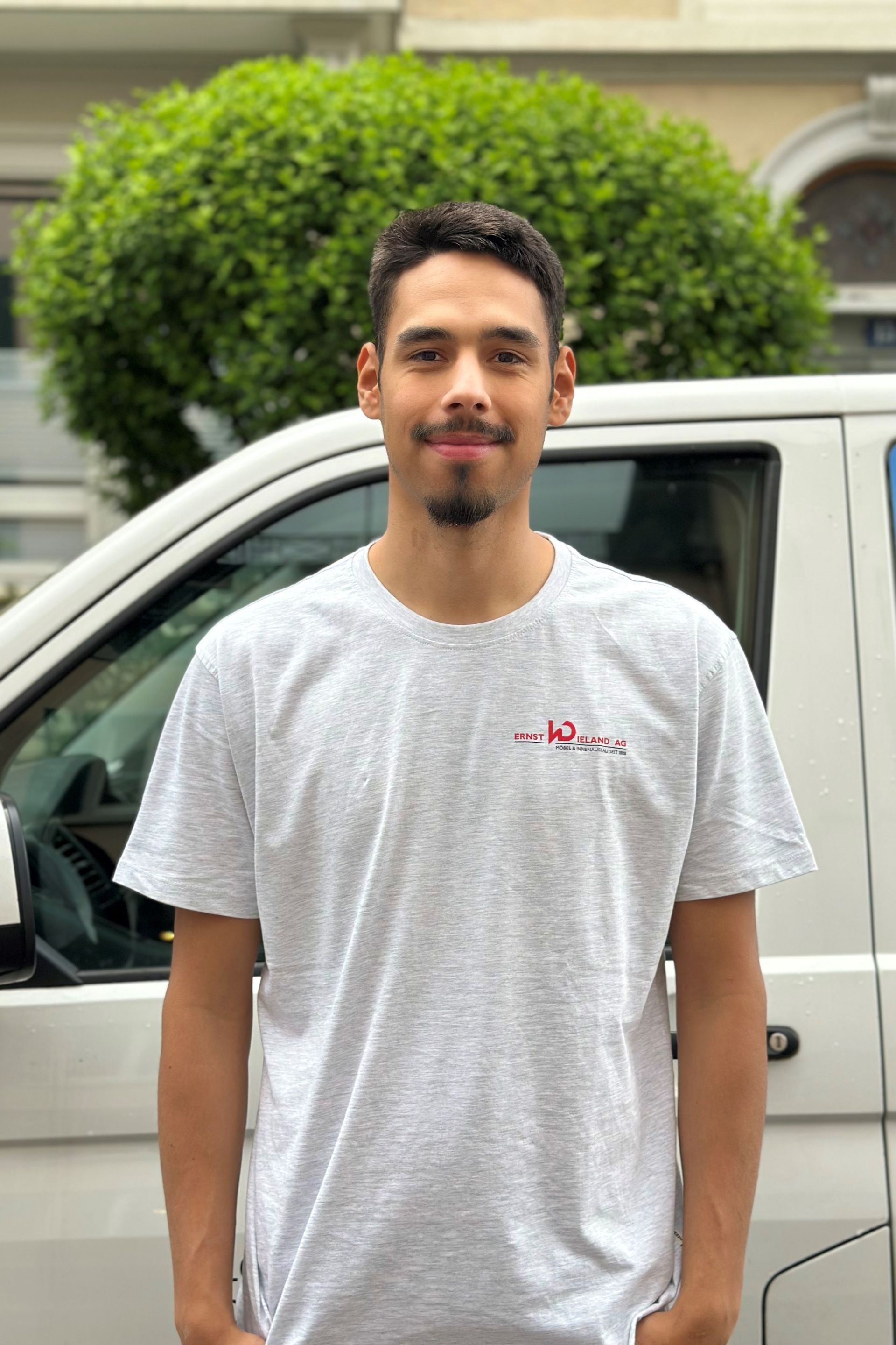 Ein Mann in einem weißen T-Shirt steht vor einem weißen Lieferwagen.