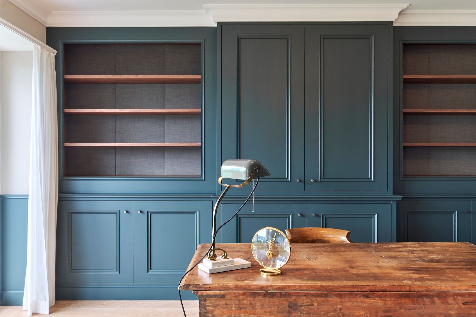 Ein Schreibtisch mit einer Lampe darauf in einem Raum mit Regalen