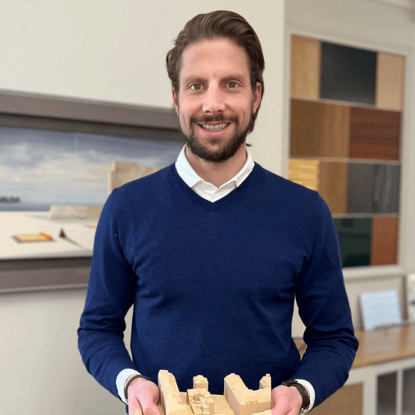 Ein Mann in einem blauen Pullover hält ein Modell eines Gebäudes