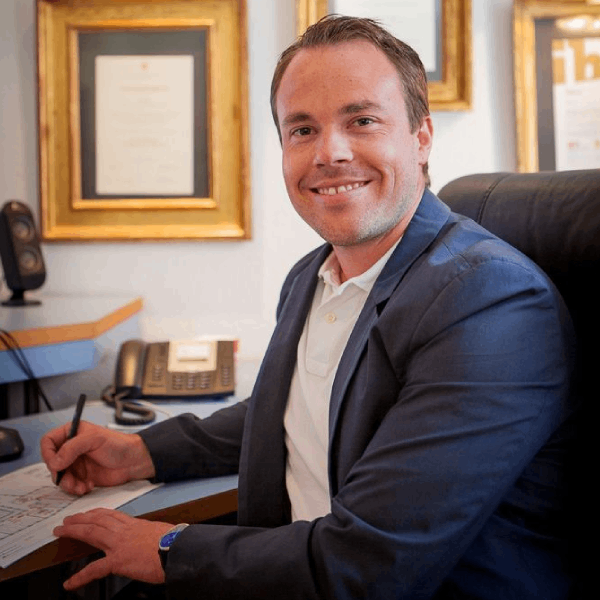 Ein Mann im Anzug sitzt an einem Schreibtisch und schreibt auf ein Stück Papier