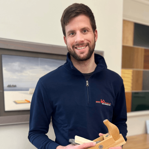 Ein Mann im blauen Hemd hält ein Holzflugzeug