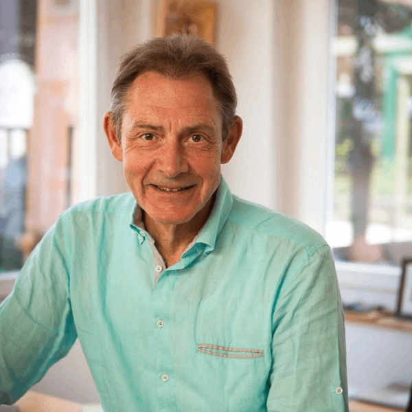 Ein Mann in einem blauen Hemd sitzt an einem Tisch und lächelt.