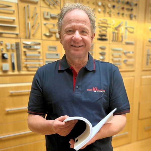 Ein Mann hält ein Buch mit Griffen vor einer Wand