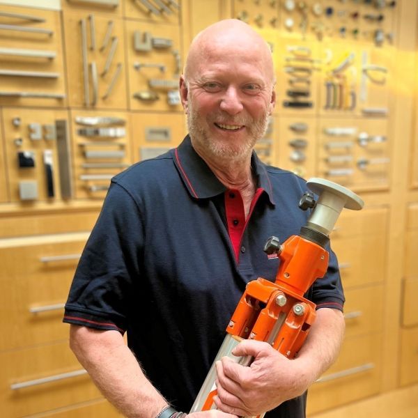 Ein Mann in einem blauen Hemd hält ein orangefarbenes Stativ