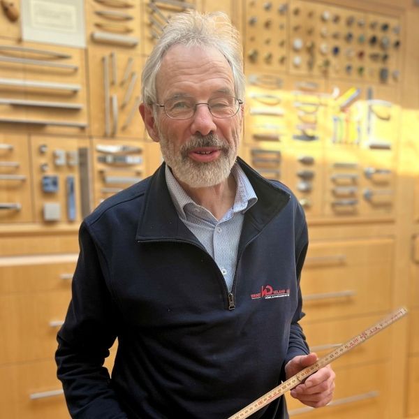 Ein Mann mit Bart und Brille hält ein Maßband.