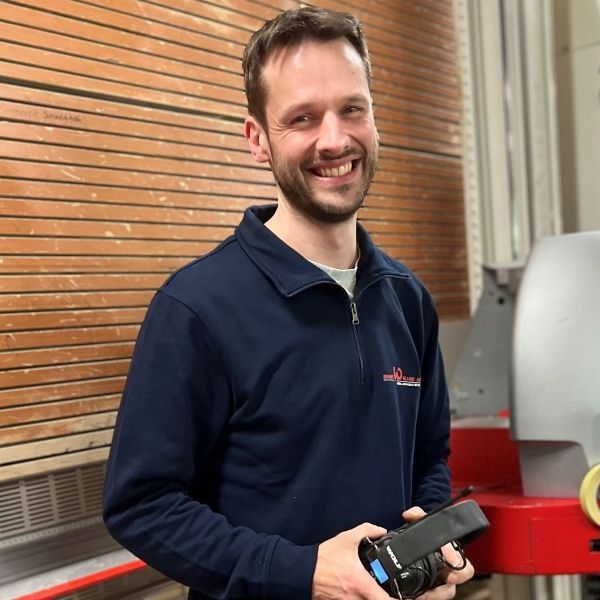 Ein Mann in einem blauen Hemd hält eine Kamera und lächelt